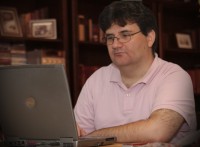 Faludi Zsolt �l egy k�nyvespolc el�tt �s egy sz�rke laptopot n�z